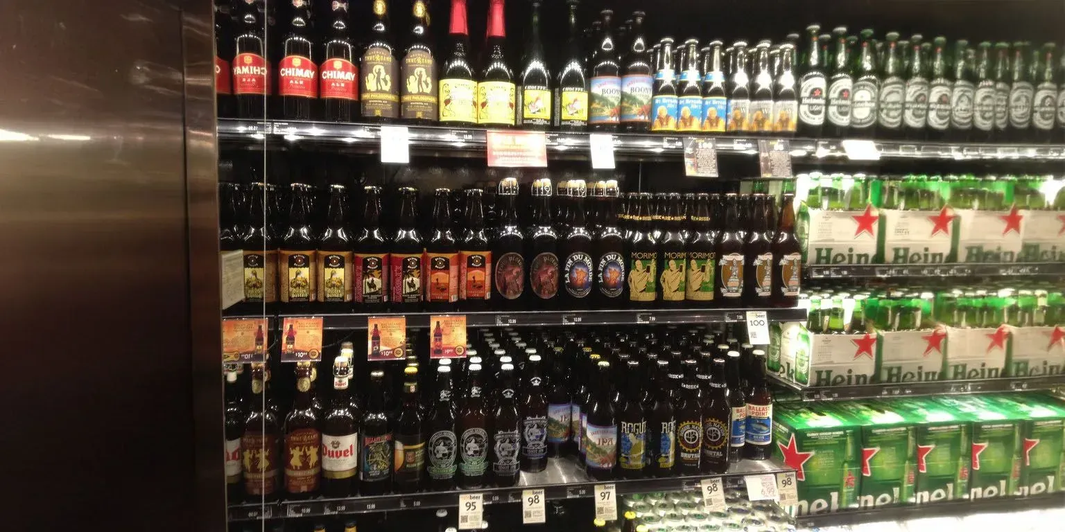 Beer bottles in a refrigerated display case in a store. Variety of brands, and packaging.
