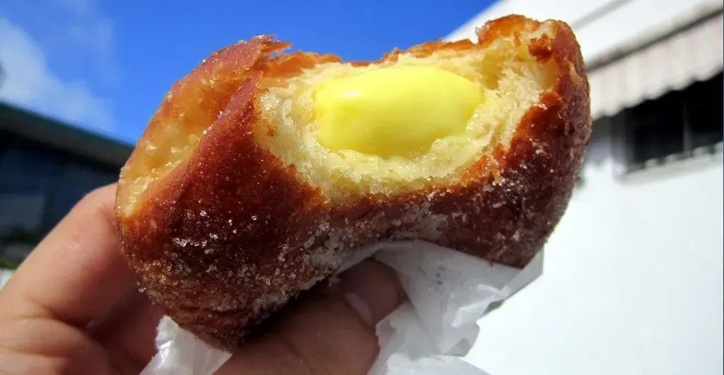 A person is holding a donut with a bite taken out of it.